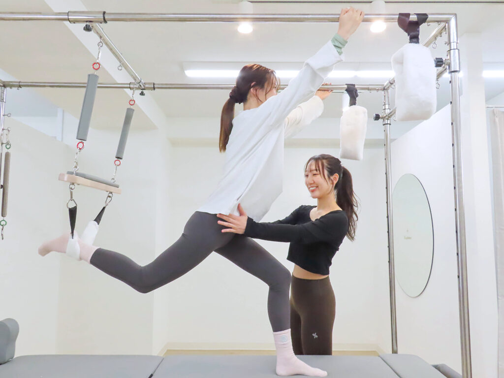 インストラクターからリフォーマーを使ったピラティスレッスンを受けている女性